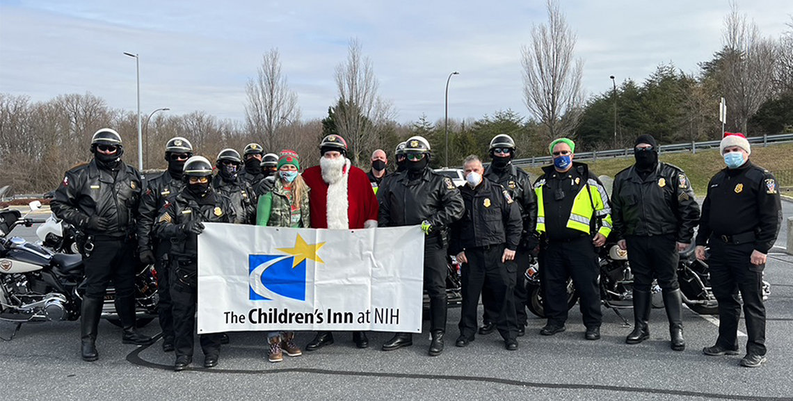 A large group of officers, dressed in black with helmets, stand with Santa, also in a helmet, and their motorcycles on the side of the road.