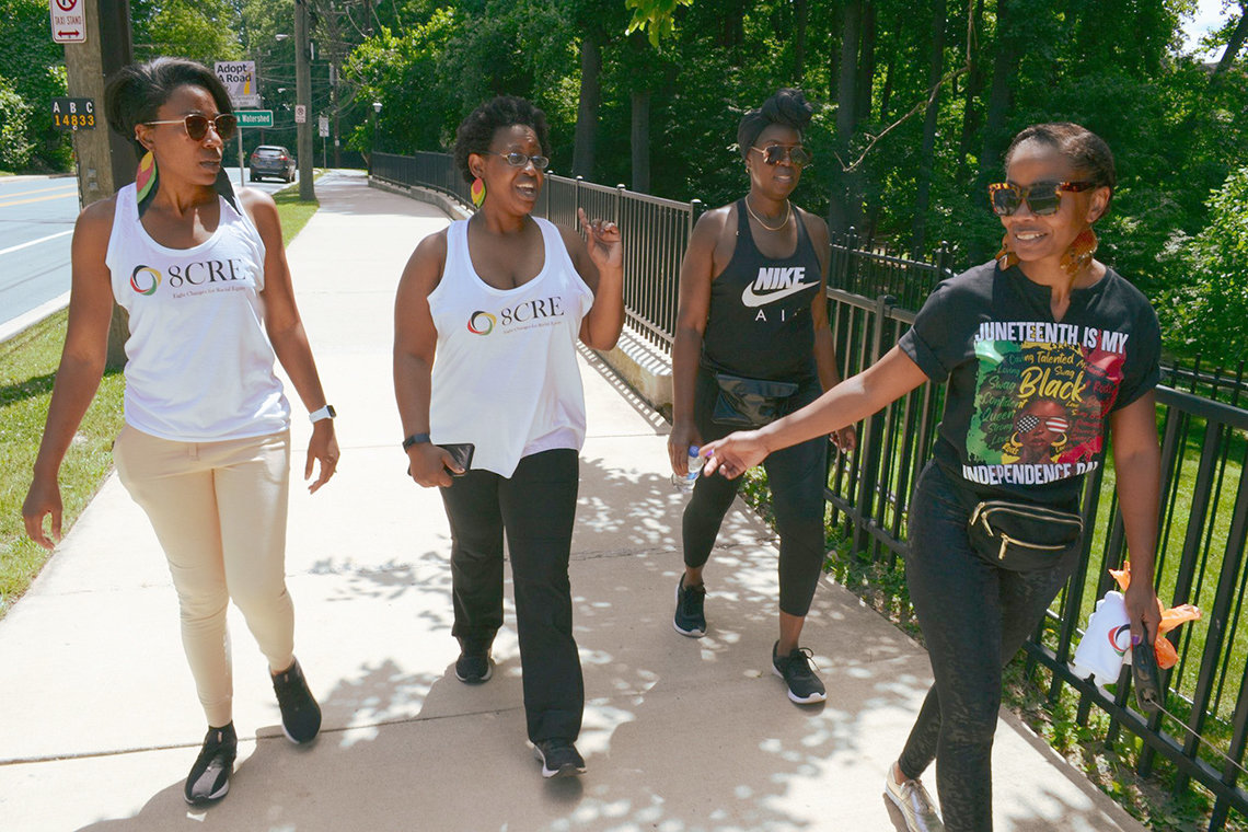 Four women in T shirts, workout pants, and sneakers walk along paved path