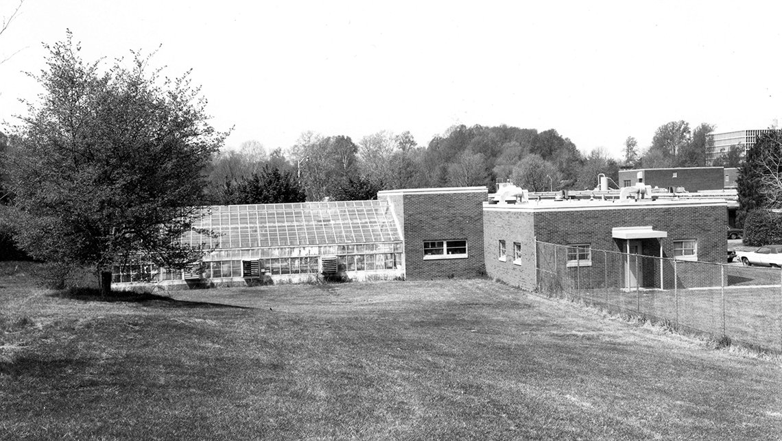 A greenhouse connects to a building annex on the lawn in this black-and-white photo.