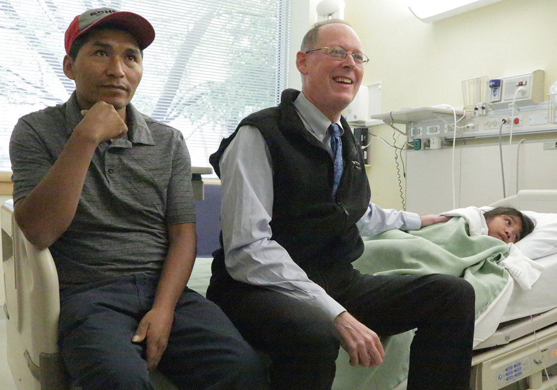 Farmer sits on the hospital bed with patient Melva, 7, and her father Carlos in the Clinical Center.