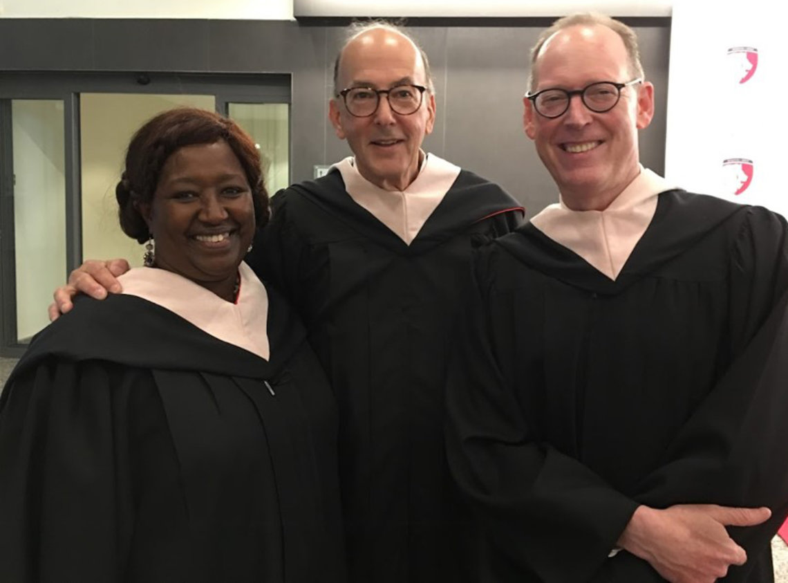 UGHE vice chancellor, Glass and Farmer, stand smiling shoulder-to-shoulder, in black graduation gowns and white collars.