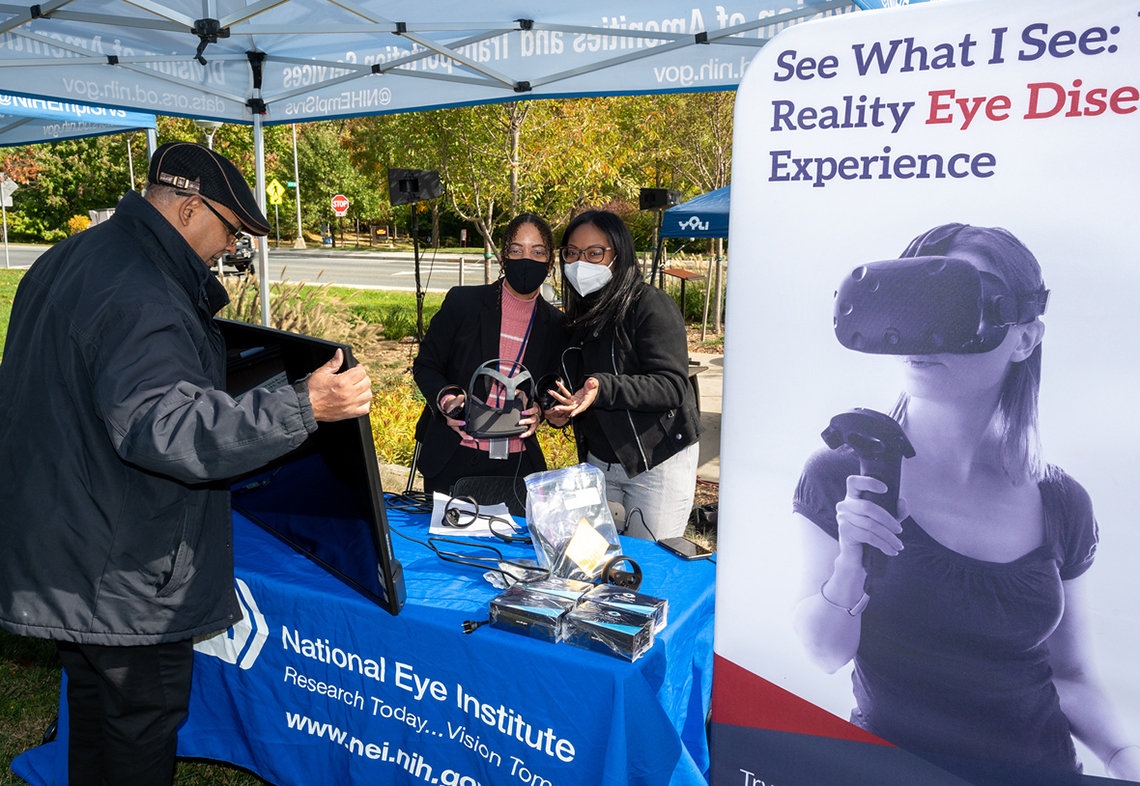 A man visits the NEI virtual reality table; a banner reads: "See what I see: reality eye disease experience"