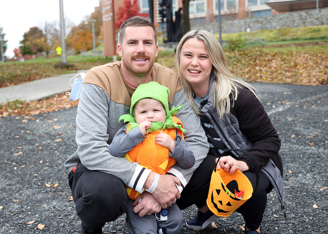 Youngster dressed as a jack o'lantern stands as dad and mom squat for photo