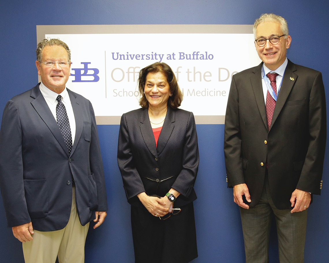 D’Souza stands between two men in front the University of Buffalo School of Dental Medicine logo