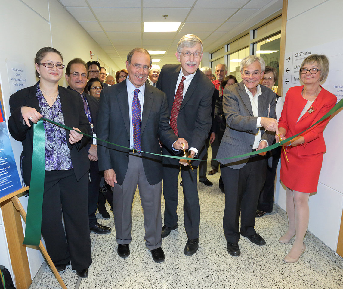 Five individuals smile at camera as they cut a ceremonial ribbon in a Clinical Center corridor