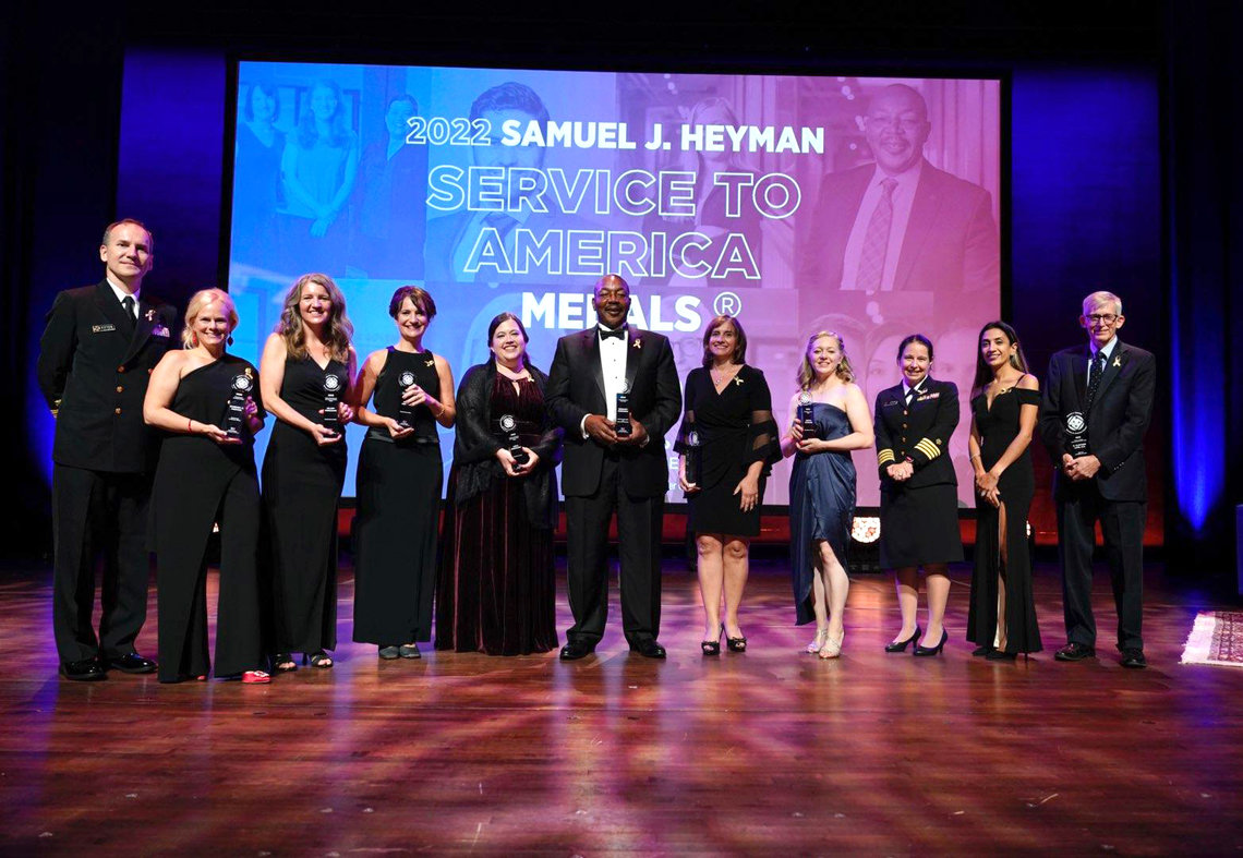 Winners stand on the stage with their trophies in front of a screen that reads 2022 Samuel J. Heyman Service to America Medals 