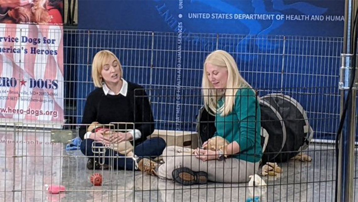 Weber and Quinlan sit by dog crate, each holding a sleepy puppy.