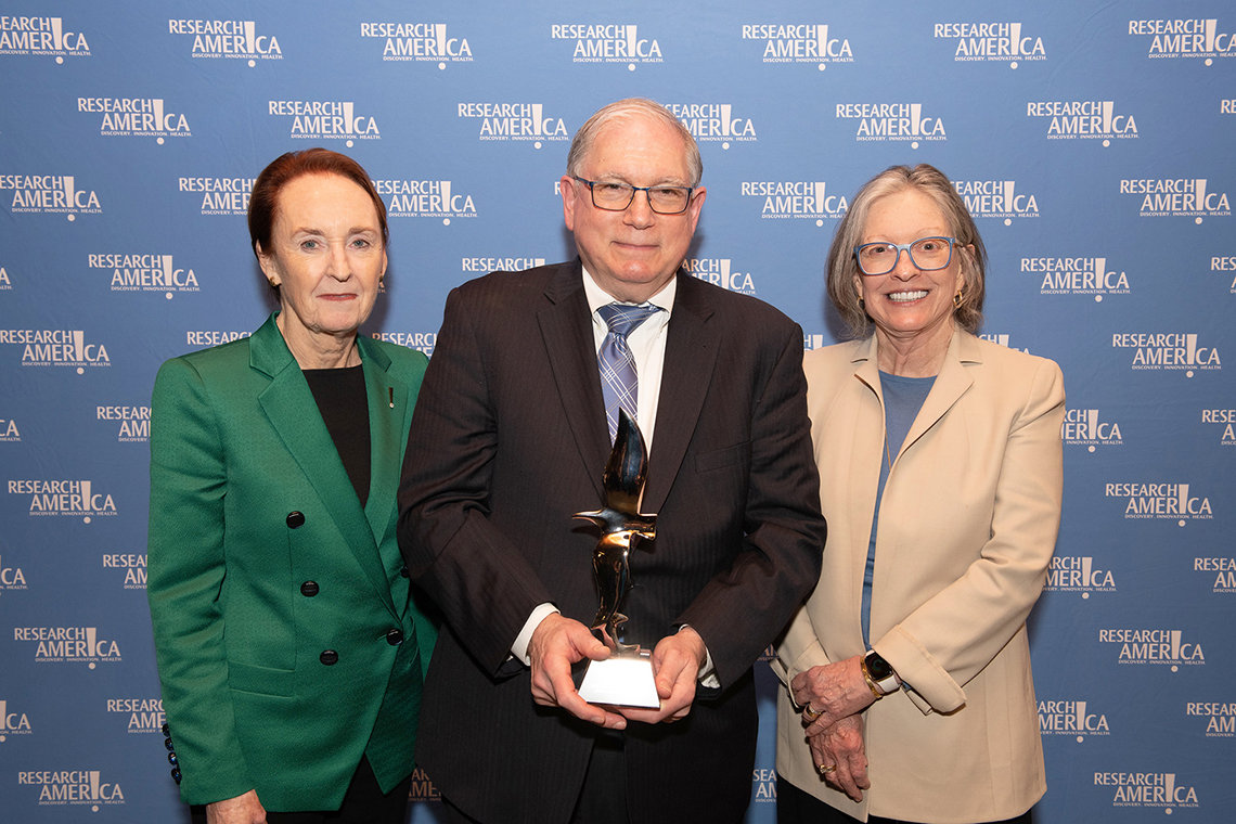 Mary Woolley and Ann Lurie stand with Dr. Tabak, who is holding award, against Research!America backdrop.