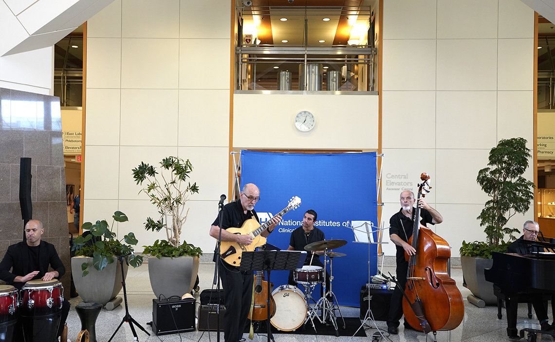A quintet--playing congas, guitar, drums, upright bass and piano--perform in the Clinical Center atrium.