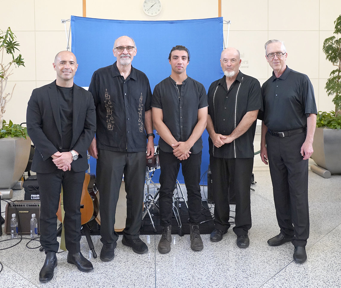 The five musicians stand, posing together, all dressed in black.
