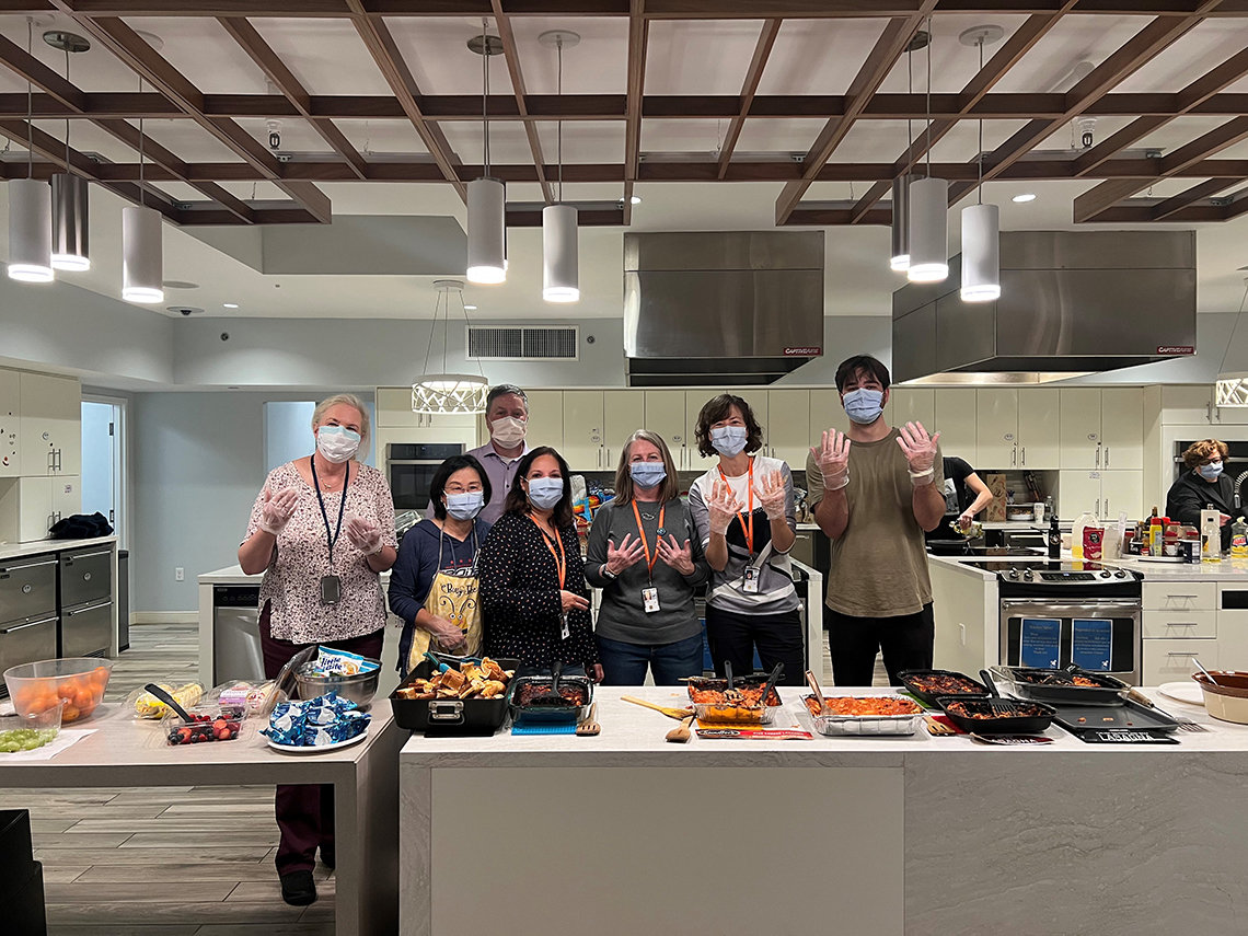 Seven staffers in face masks and gloves gesture toward the camera