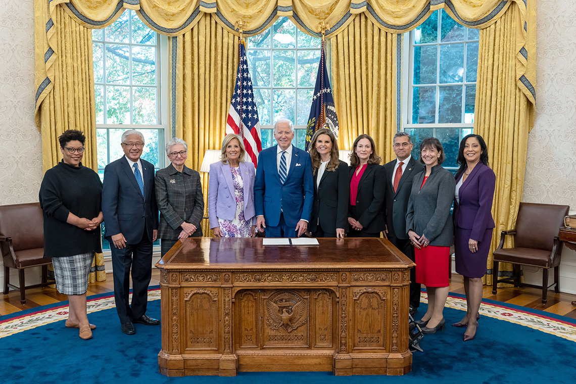 President Joe Biden and First Lady Dr. Jill pose with women's health advocates behind desk in Oval Office.