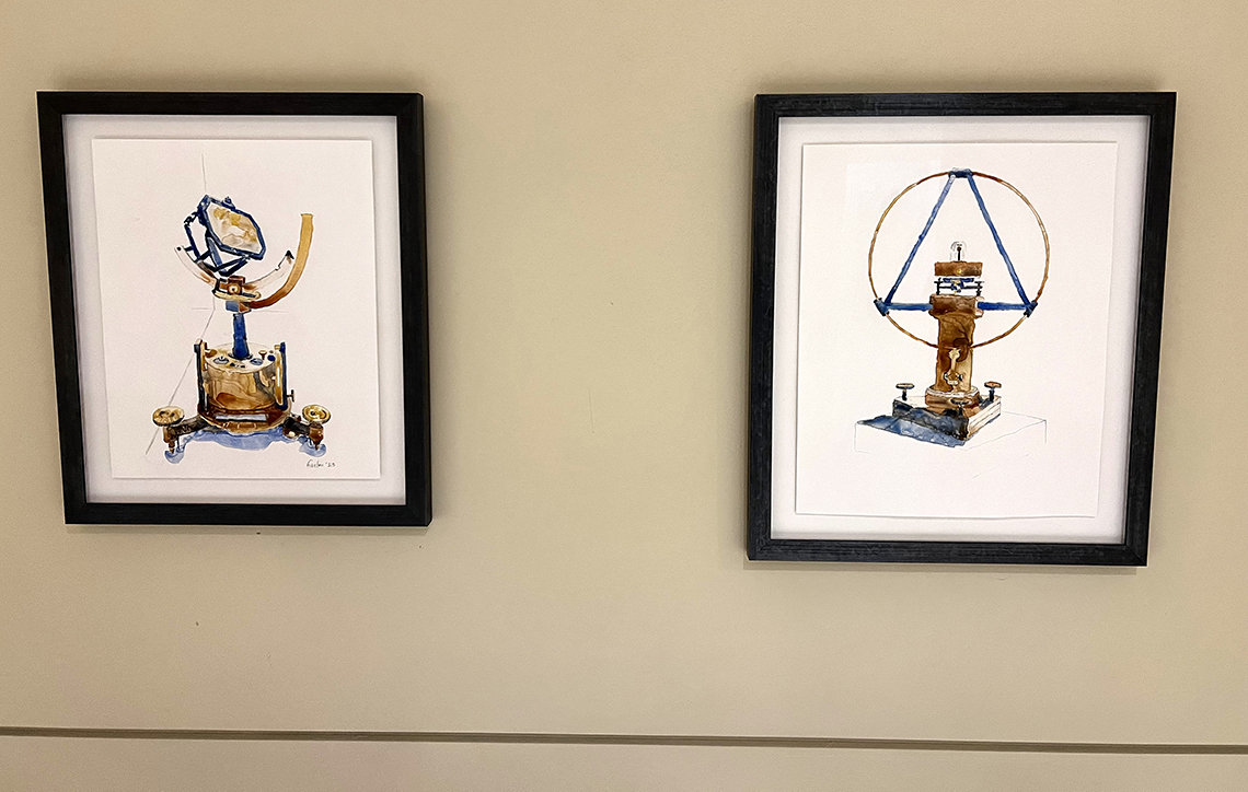 Two framed watercolors of scientific instruments, installed on wall