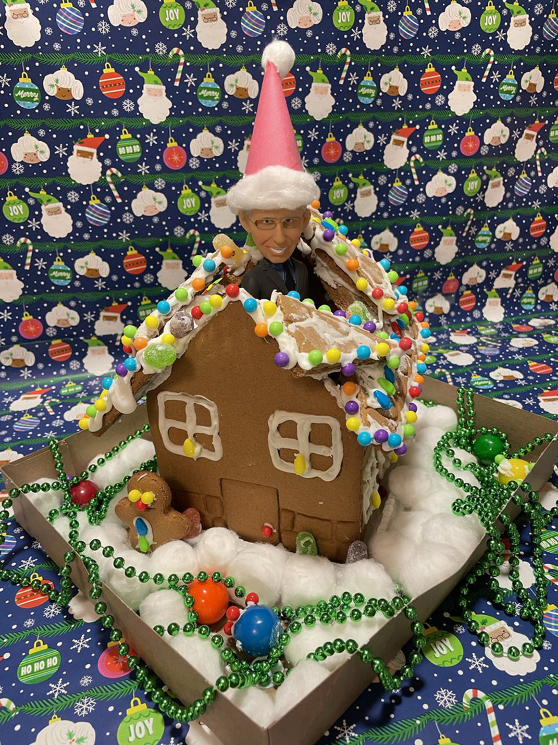 A Dr. Fauci bobblehead pops out of a gingerbread house