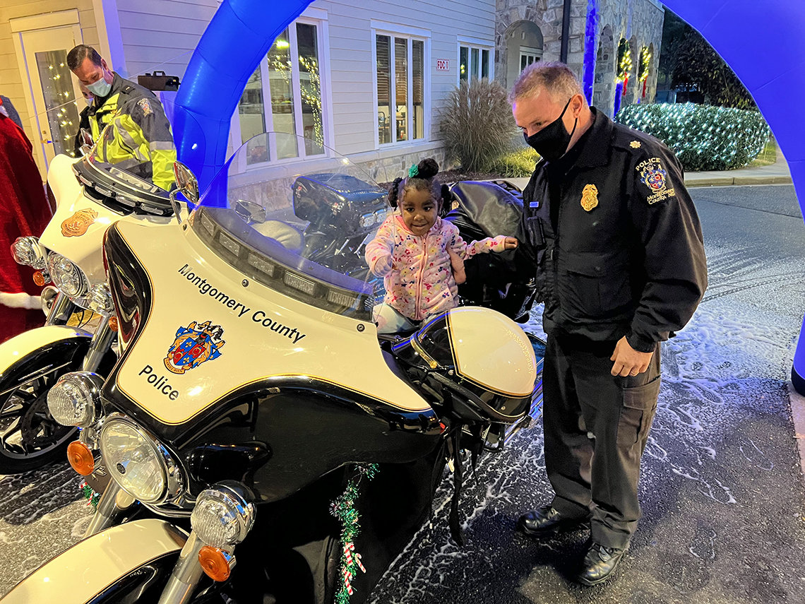 An officer watches a baby who is sitting on a motorcycle