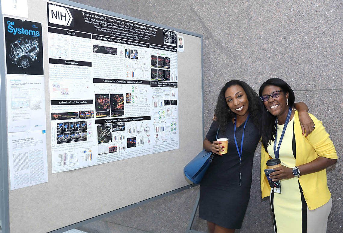 Two smiling attendees stand by scientific poster.