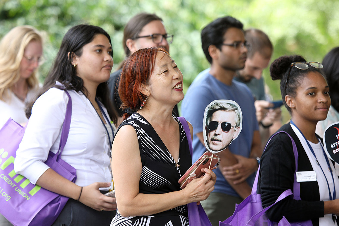 Close up of concert-goer holding band fan illustrated with Francis Collins face wearing sunshades.