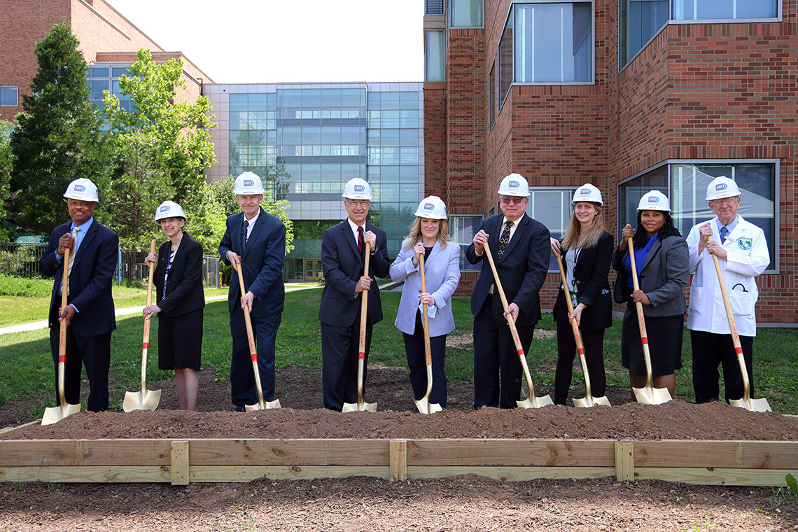 NIH leadership wear hard hats and hold golden shovels during the ceremony 