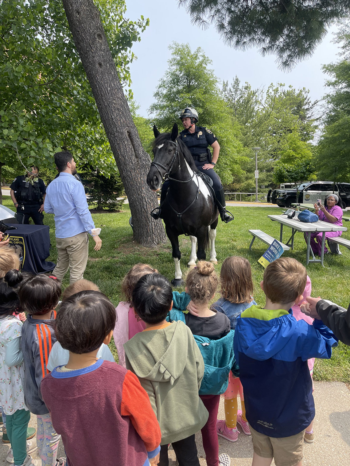Officer on a horse, as kids and a man look on.