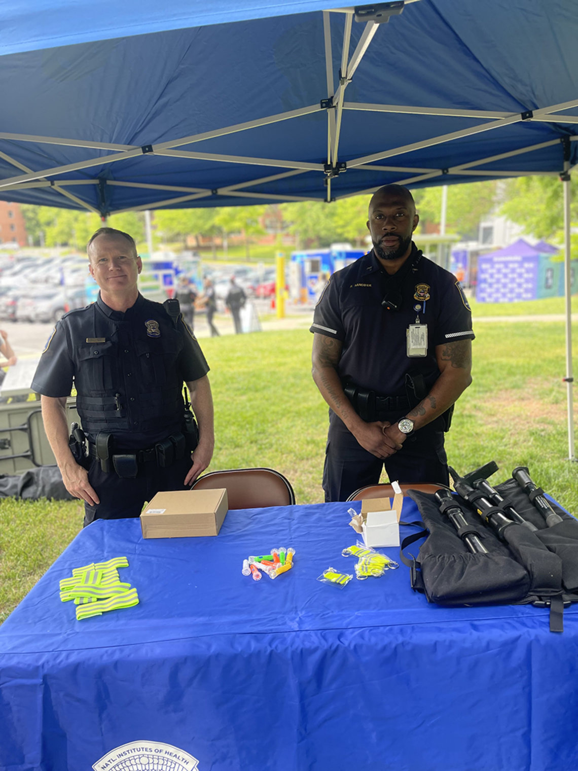 Two uniformed police officers stand at information table under blue tent.