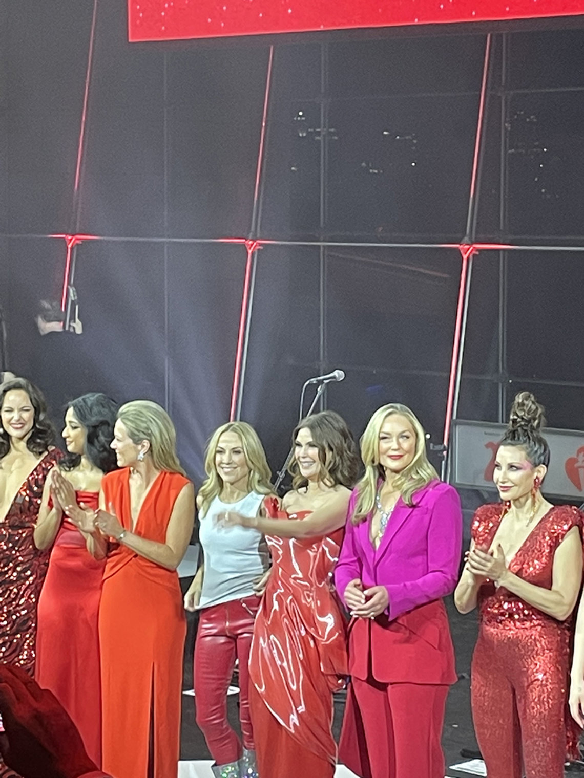 A group of women in red and pink attire stand on stage.