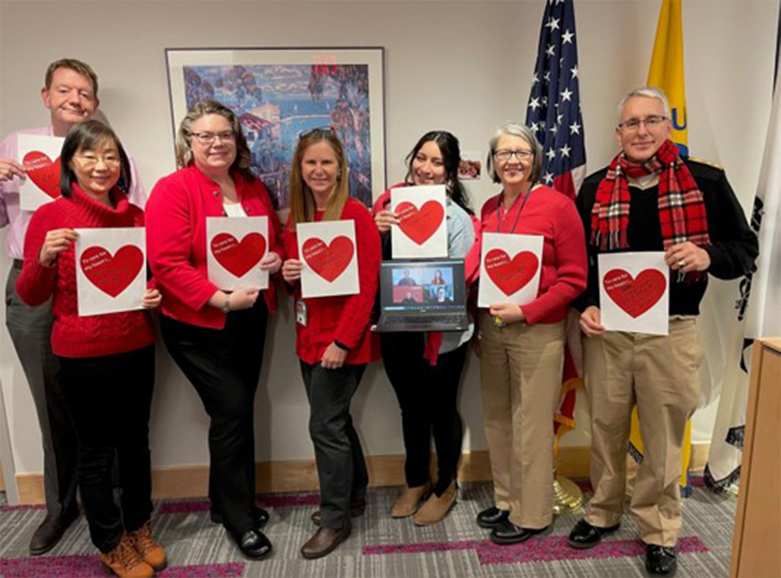 Seven NIH'ers stand holding red hearts with their healthy pledges written inside.