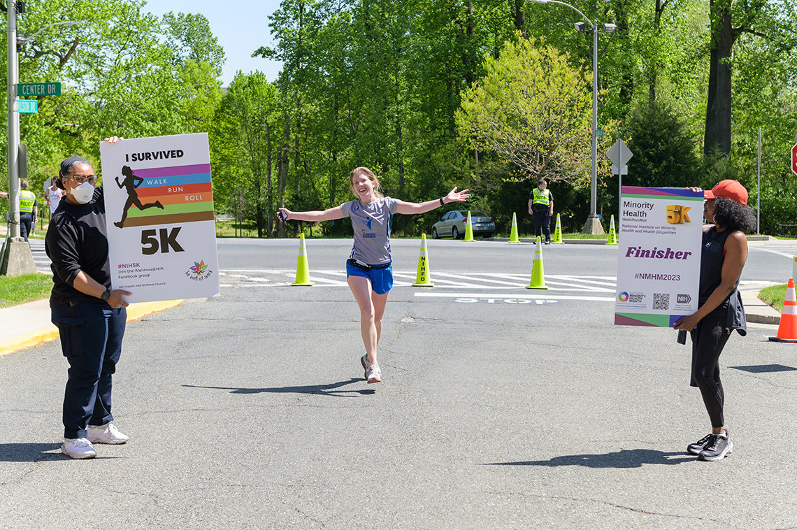 A runner holds arms outstretched in victory as she approaches the finish line; staff hold banners reading: I survived the 5k