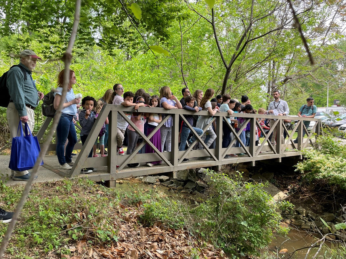 Price speaks to a group of children and their parents on a bridge above the NIH stream