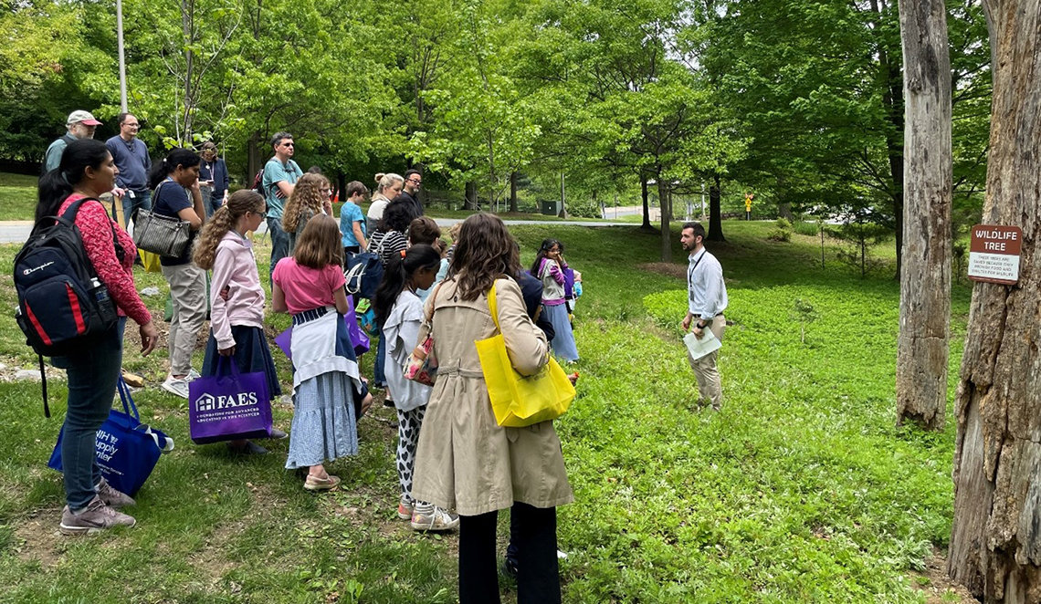Price speaks to a group of children and their families in a clearing on campus