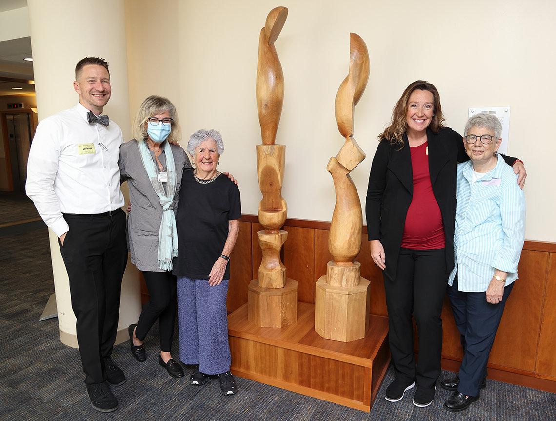 A man and four women stand alongside a sculpture featuring 2 wooden towers