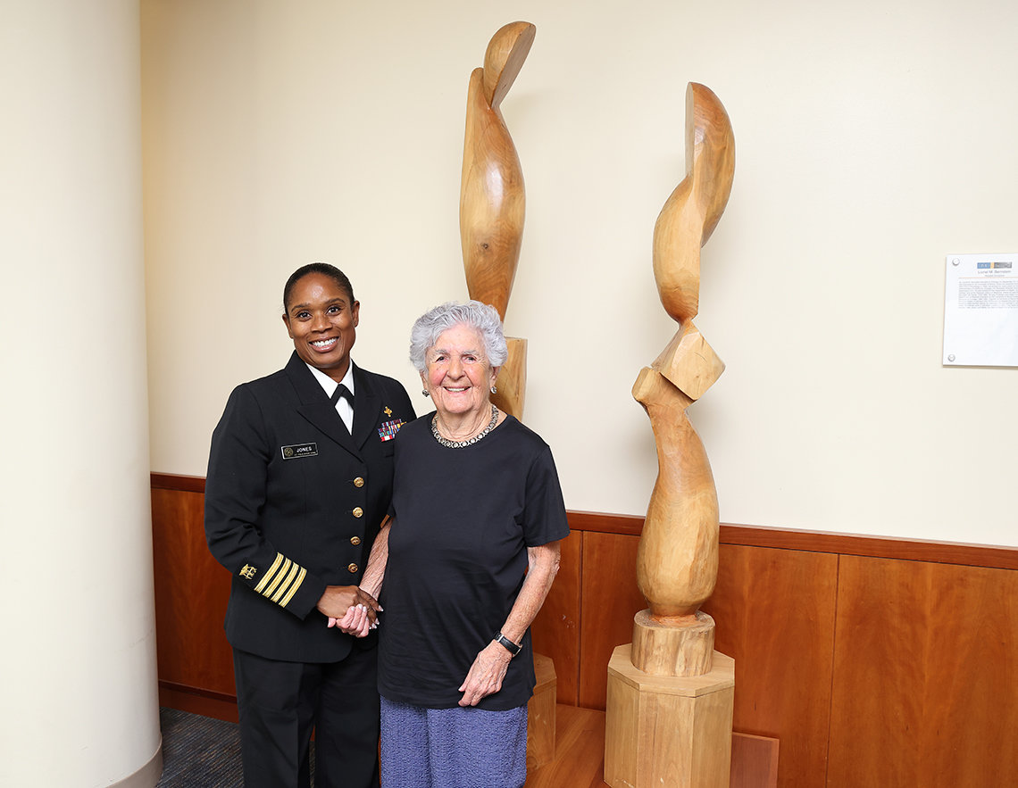Two women, one African American and in PHS uniform, stand beside a wood sculpture