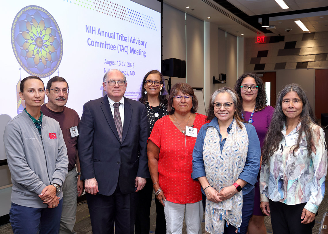 Tabak and participants pose in front of screen that reads: NIH Annual Tribal Advisory Committee Meeting