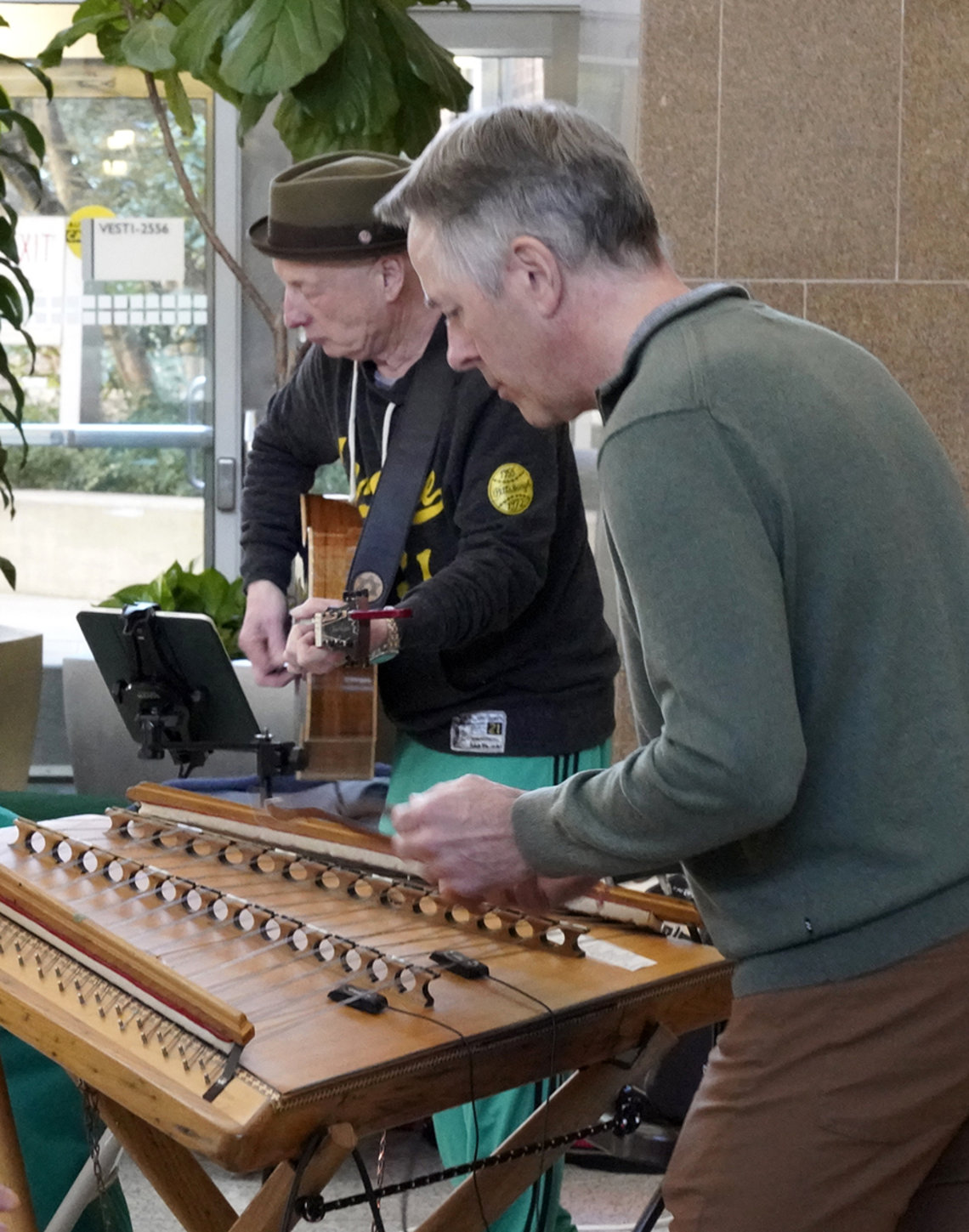 A man plays the hammered dulcimer. Another man plays the guitar in the background.