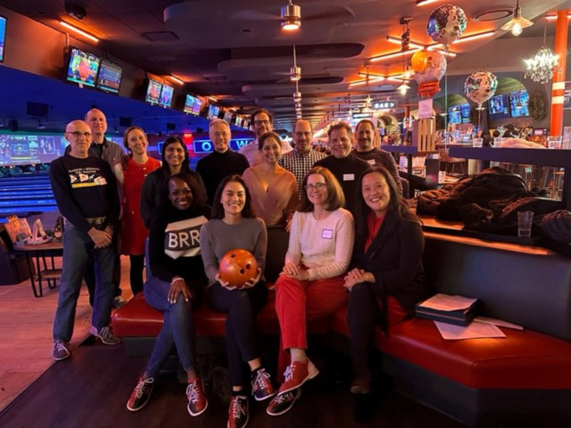 The group poses for a photo at the bowling alley. An attendee in the front row holds an orange bowling ball.