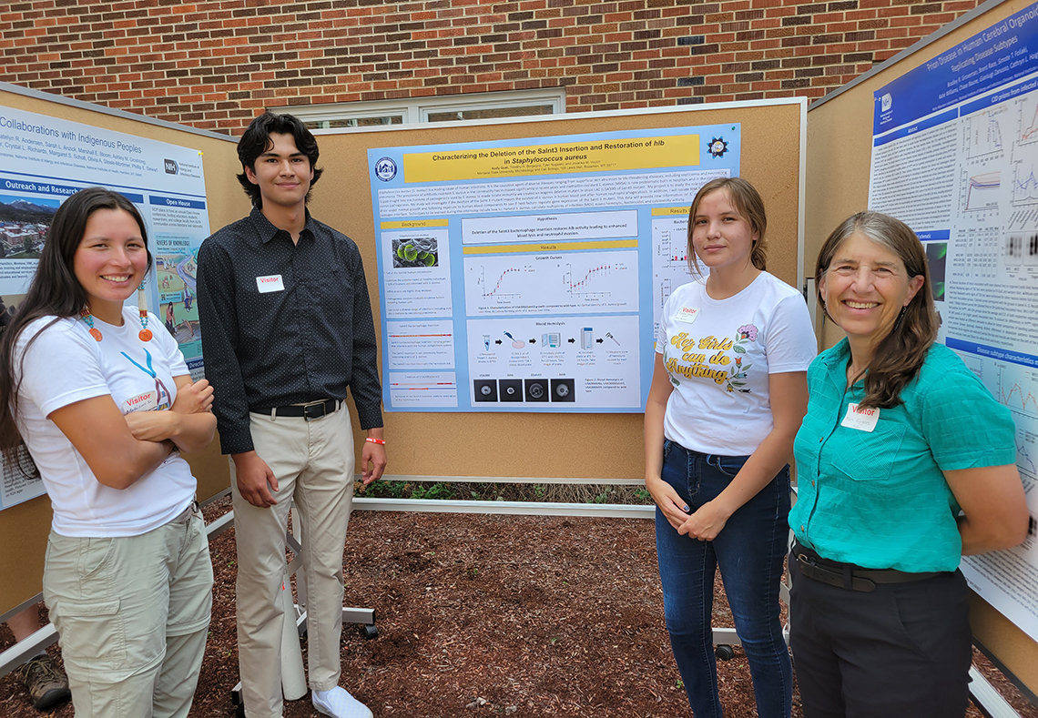 American Indian students and a faculty member pose in front of scientific posters in a courtyard on the RML campus.