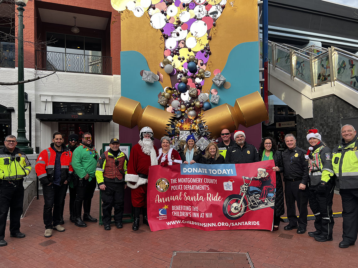 A group photo featuring Inn staff and police officers holding a banner advertising the Santa Ride
