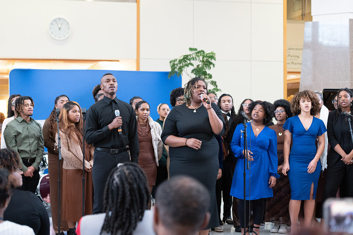 Large group singing with Black man and Black woman in front with handheld mics.