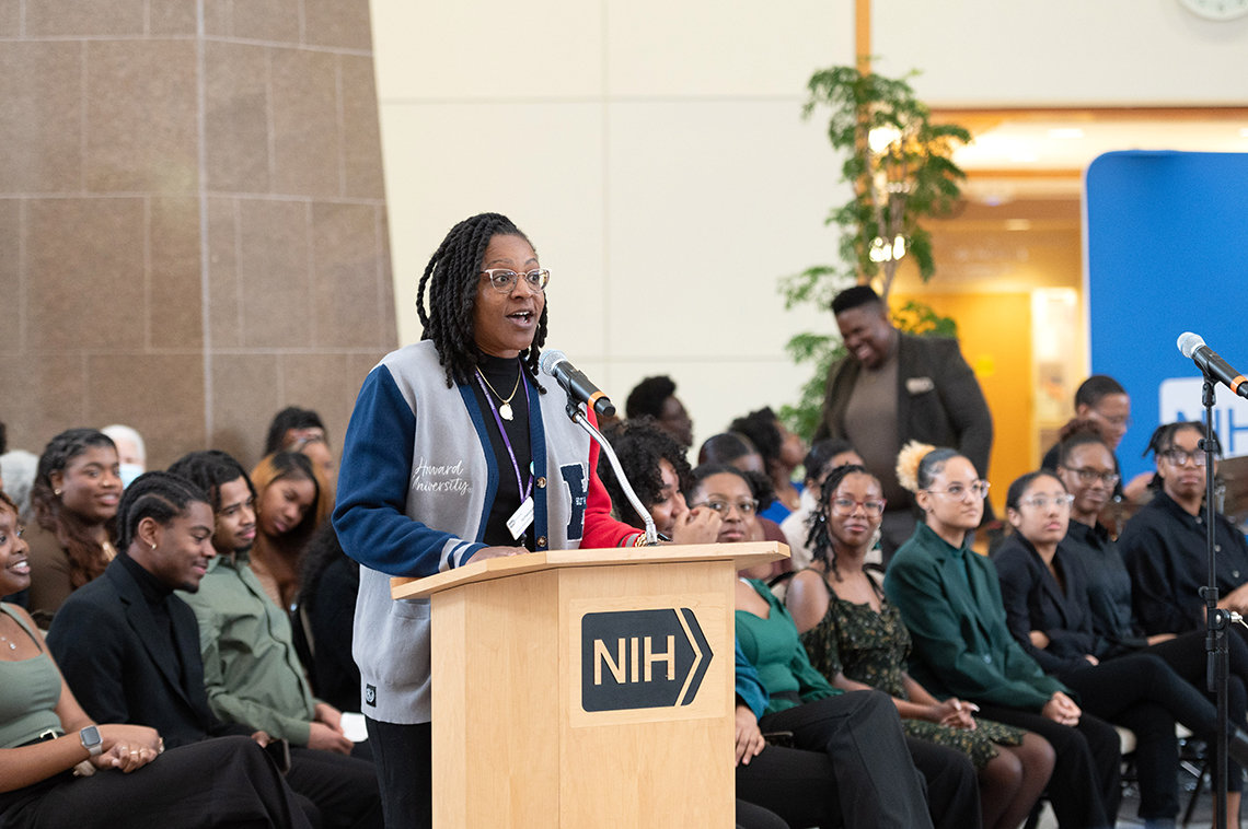 Black woman at NIH podium wears a Howard University logo sweater.
