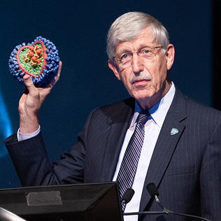 Collins holds up a flu virus model at the podium.