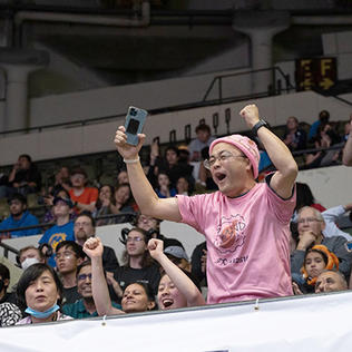 Man in pink T shirt and pink skullcap raises arms and yells 