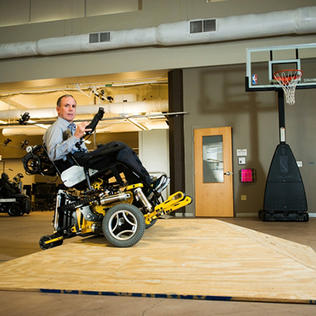 Cooper in MEBot power wheelchair, in gymnasium with basketball hoop