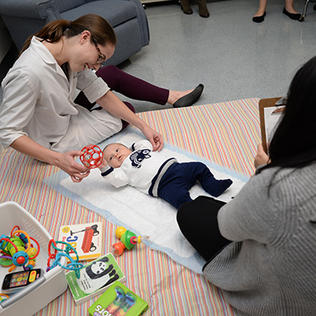 A researcher plays with a baby who is laying on its back 