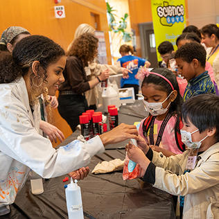 Scientist in white lab coat hands a bag of slime to kids.