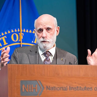 Cerf gestures at the podium, with Public Health Service flag behind him.