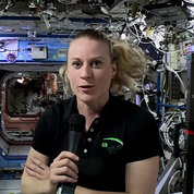Dr. Kate Rubins talks into microphone inside space station, surrounded by wires and equipment.