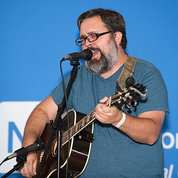 Milner playing guitar and singing at microphone