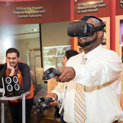 A man holds out, moves handheld device and wears head gear to try virtual reality experience in Clinical Center south lobby.