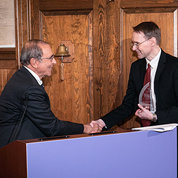 Gallin shakes hands with awardee Kochenderfer at podium draped with purple FNIH banner.
