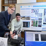 Tromberg and Monroy manipulate an imaging device as Hammer views screen, with scientific poster behind them. 