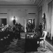 Nixon signs the act in a front of a crowd in a White House room